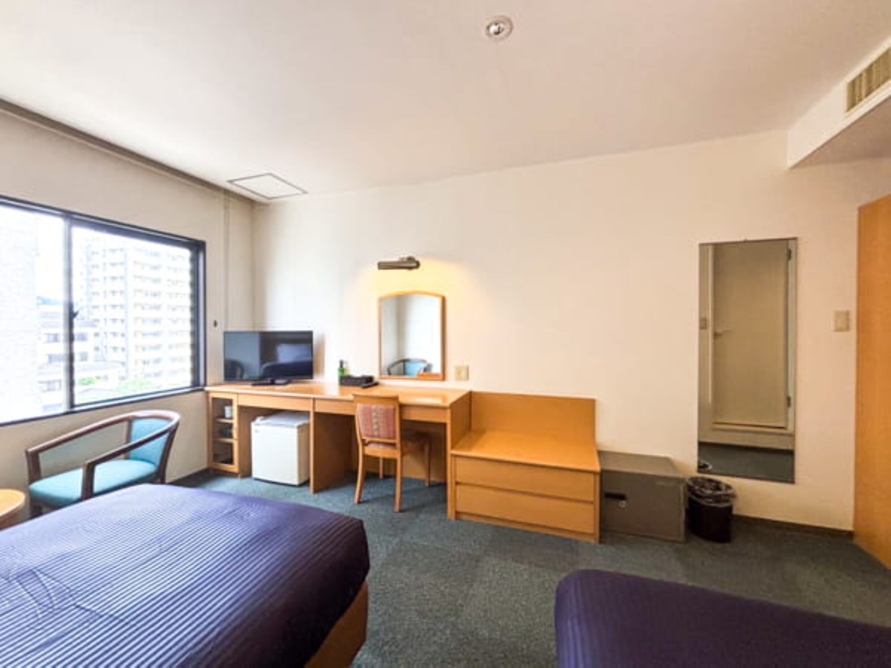 A hotel room with a bed, desk, chair, television, and a window.