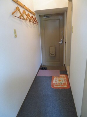 Ein schmaler Flur mit einer Tür am Ende, einem Schuhregal an der Wand und einem kleinen Teppich auf dem Boden.
