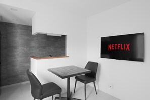 Una habitación moderna con una televisión de pantalla plana, una mesa, dos sillas, una encimera de madera y una pared oscura.