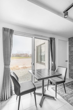 Ein modernes Zimmer mit Glastür und Blick, einem Tisch mit Stühlen und einem grauen Teppich.