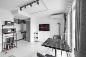 Eine moderne Küche mit Mikrowelle, Backofen und Kaffeemaschine auf einem Wagen, einem Esstisch mit Solarmodul, einem Fernseher, der 'NETFLIX' zeigt, und einem Fenster mit Vorhängen.