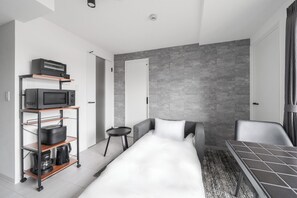 Quarto de hotel moderno com cama, uma pequena mesa, sofá, máquina de café e micro-ondas em uma prateleira.