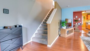 A staircase leading to a second floor, a dark wooden dresser, and a kitchen area with a red accent wall.