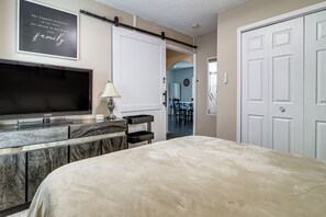 A bedroom with a bed, a TV, a desk, and a door.