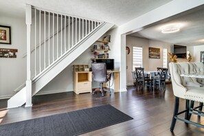 A staircase with white railings, a desk with a computer, a dining table with chairs, and a decorative chair.