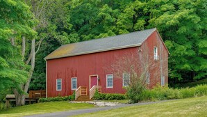 A red barn with a wooden staircase leading to a door, surrounded by lush greenery and trees. - Guest House w/ Private Pond & Dock in Southbury! (Southbury)