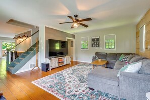 Ein Wohnzimmer mit grauem Sofa, einem gemusterten Teppich, einem Deckenventilator und einer Treppe.