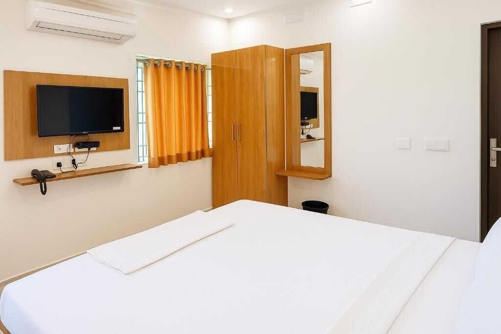 Una habitación de hotel con cama, televisor montado en la pared, armario y espejo.
