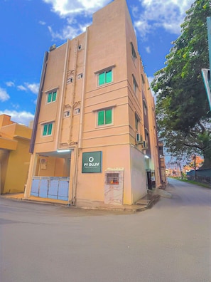 A multi-story building with a sign for 'Py Olliv' on the ground floor, a gated entrance, and a clear sky in the background.