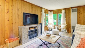 Een kamer met houten lambrisering, een open haard, een televisie, rieten stoelen en een bank.