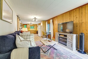 Ein Wohnzimmer mit Sofa, Fernseher, Kamin und einer Küche im Hintergrund.