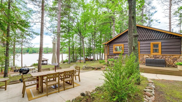 Een chalet met een terras, buitenmeubels, een barbecue en uitzicht op een meer.