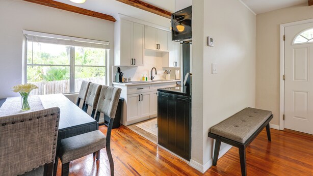 A kitchen with white cabinets, a black refrigerator, wooden beams, and a dining area with a table and chairs.