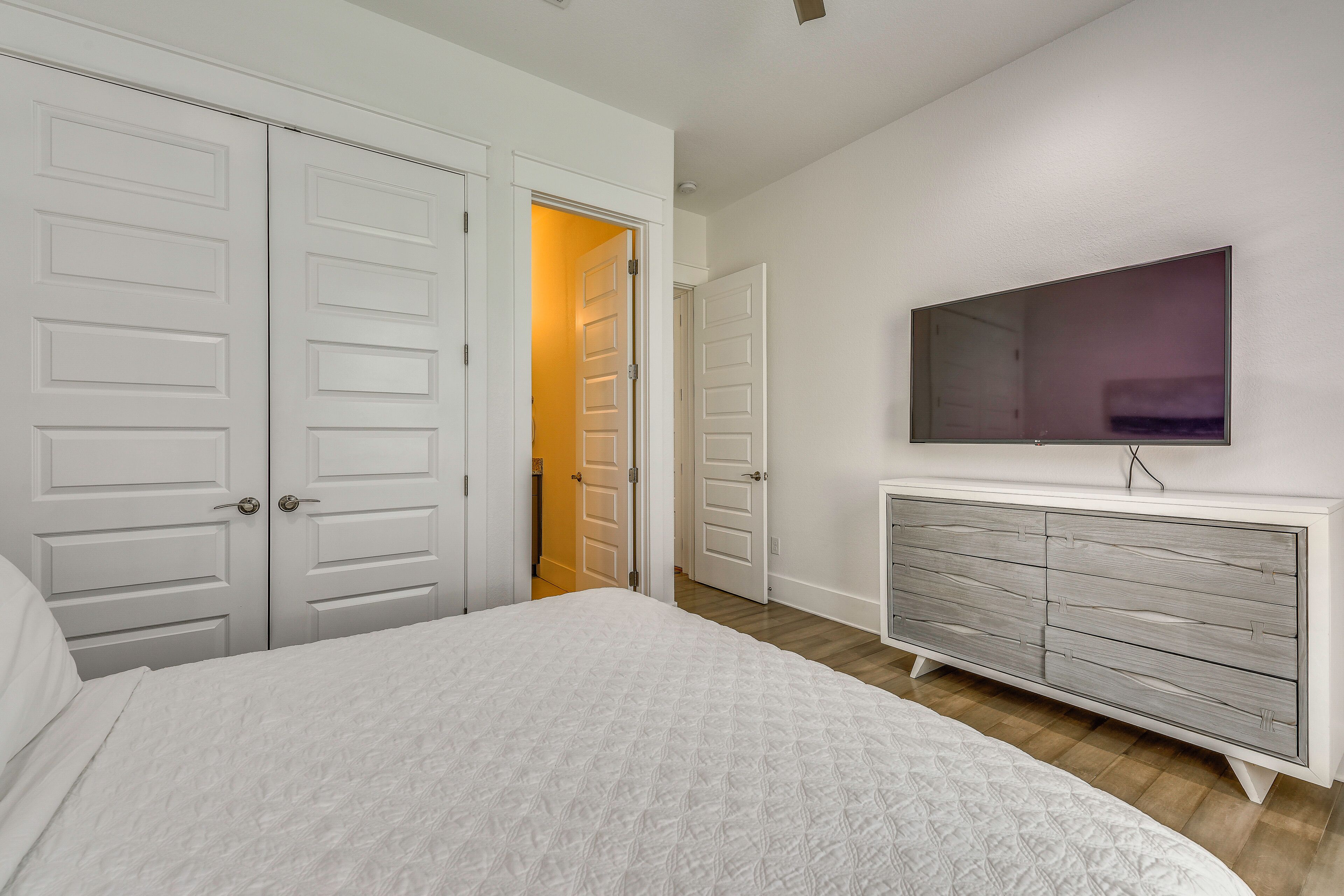 A bedroom with a bed, a dresser, a television, and a hallway leading to another room.