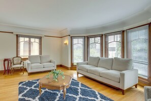 Un salon comprenant un canapé, un fauteuil, une table basse et de grandes fenêtres équipées de stores.