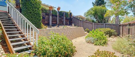 A residential backyard with a wooden staircase, a brick wall, and various plants.