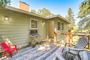 A wooden deck with two Adirondack chairs, a grill, and a small table.