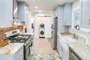 A modern kitchen with a gas stove, oven, and built-in appliances, leading to a laundry area with a washing machine and dryer.