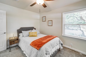 A bedroom with a bed, a nightstand, a ceiling fan, a window, and a door.