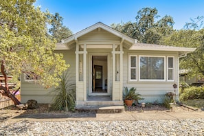 A single-story house with a front porch, a visible door, and a small front yard with gravel and plants.