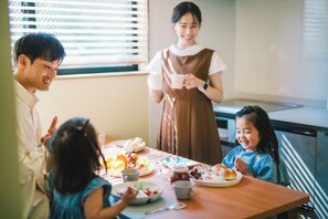 Una mesa de comedor con comida y bebidas, una persona de pie y otra sentada.