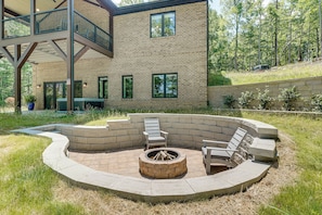 Un espace extérieur circulaire aménagé avec des sièges, doté d’un foyer, entouré d’escaliers et de bancs en pierre, et situé à côté d’un immeuble à plusieurs étages avec un balcon.