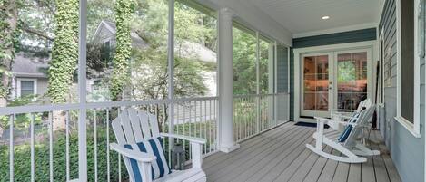 A covered porch with white railings, two Adirondack chairs, and a view of a house and trees.