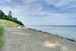 Ein sandiger Strand mit felsiger Küste, Bäumen und blauem Himmel.