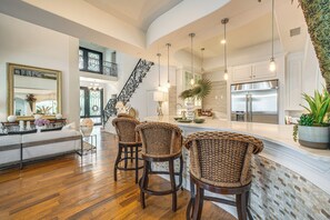 A spacious kitchen with a large island, a dining area with wicker chairs, and a staircase leading to an upper level.