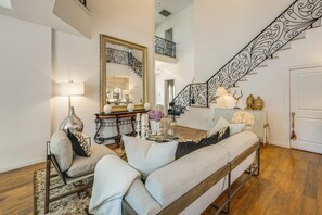 Ein geräumiges Wohnzimmer mit einer großen Couch, einem Sessel, einem Couchtisch, einem Spiegel und einer Treppe mit aufwendiger Geländering.