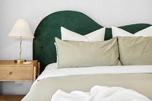 Un lit bien fait, avec une tête de lit verte, une table de chevet avec une lampe et une commode en bois.