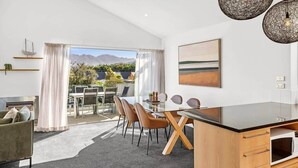 A modern kitchen with a dining area, large windows, and a view of mountains. - Alpine Four with Views (Wānaka)
