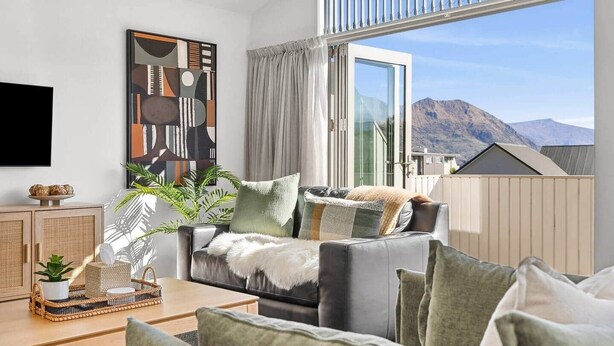 A modern living room with a sofa, a coffee table, and a large window with a view of mountains. - Alpine Four with Views (Wānaka)