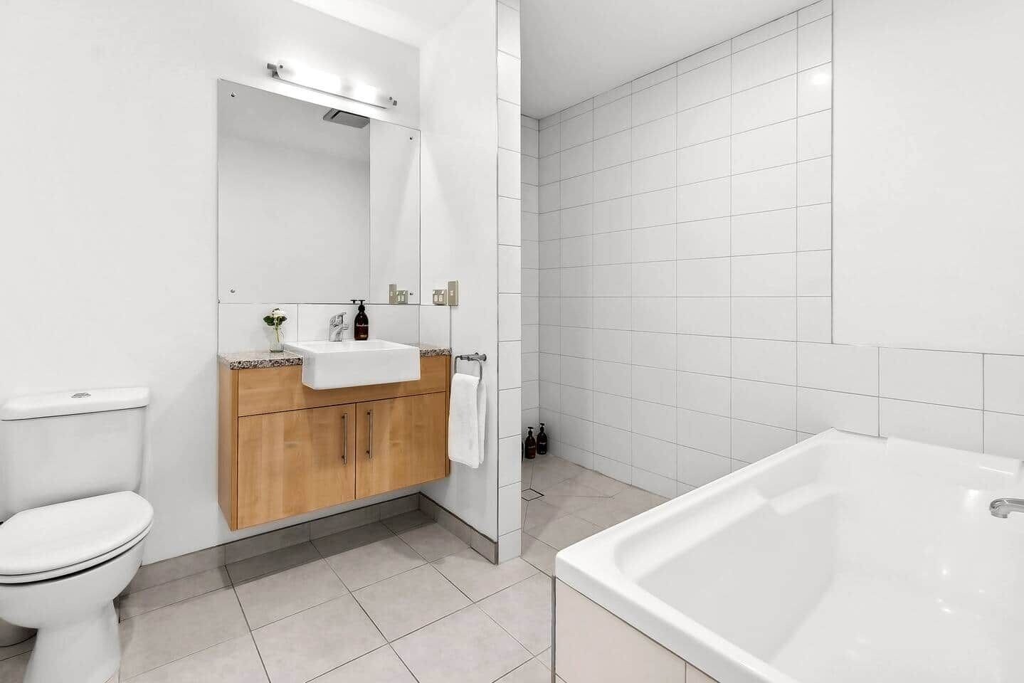 A bathroom with a toilet, sink, wooden cabinets, a mirror, a shower area, and a bathtub.