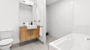 A bathroom with a toilet, sink, wooden cabinets, a mirror, a shower area, and a bathtub.