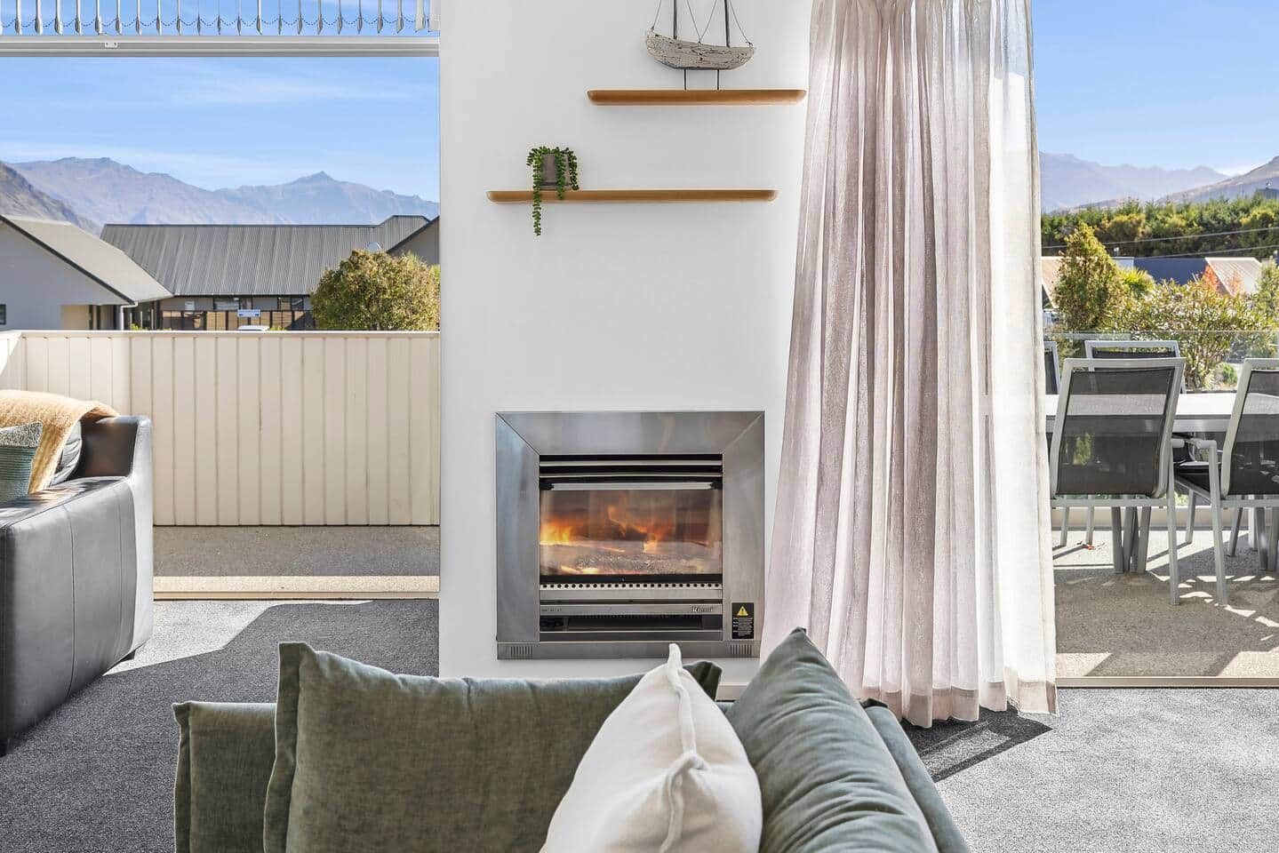 A modern outdoor living area with a fireplace, seating, and a view of mountains.