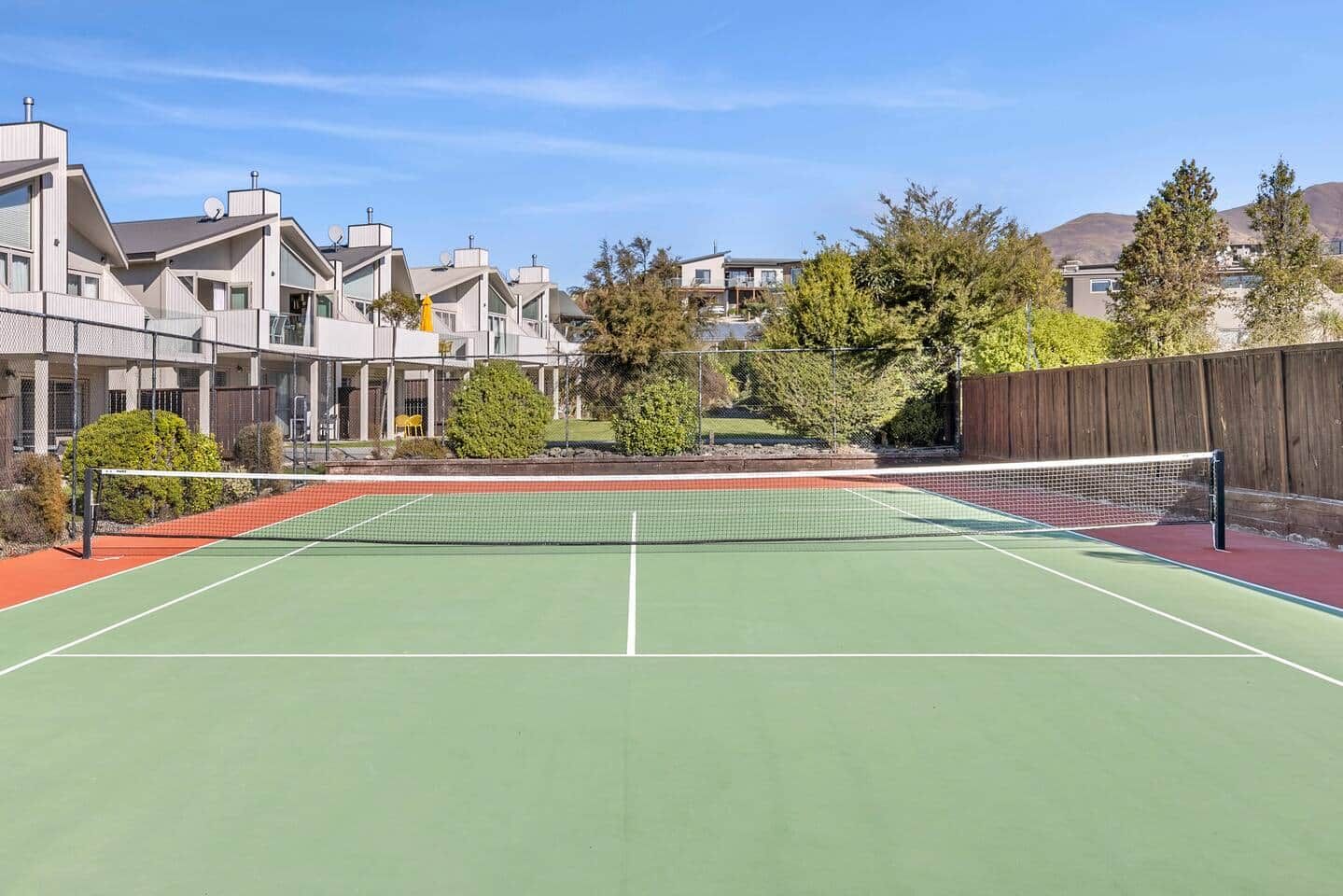 Una cancha de tenis al aire libre con una red, rodeada de edificios residenciales y árboles.