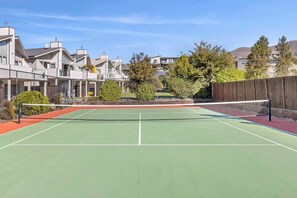 Una cancha de tenis al aire libre con una red, rodeada de edificios residenciales y árboles.