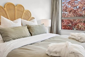 A bed with a headboard, pillows, a blanket, and a window with a view of trees. - Alpine View Apartment for Six (Wanaka)