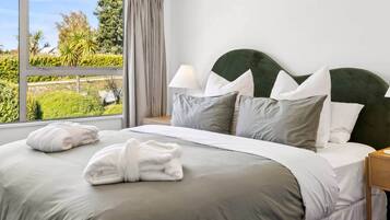 A neatly made bed with a headboard, a bedside lamp, and a view of greenery outside.