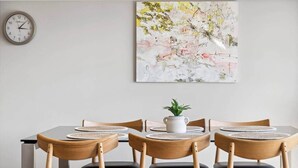 A dining area with a table set for four, wooden chairs, a clock on the wall, and a painting above the table. - Mountain Four-Guest with Views (Wanaka)