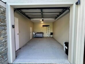 A garage with a concrete floor, a white door, a black trash bin, and a ladder leaning against the wall. - Mountain Four-Guest with Views (Wanaka)