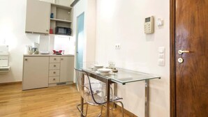 Una cocina compacta con una mesa de vidrio, sillas transparentes y una puerta de madera.