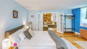 A bedroom with a large bed, a nightstand with a lamp, a dresser, and a view into an adjacent living area. - Historic South Lee Apt 2 Mi to Main Street (South Lee)