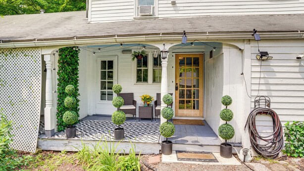 A white house with a porch, potted topiary, outdoor seating, and a garden hose. - Historic South Lee Apt 2 Mi to Main Street (South Lee)