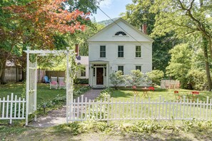 A white house with a front porch, a white picket fence, and a garden with chairs. - Historic South Lee Apt 2 Mi to Main Street (South Lee)