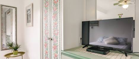Une pièce avec une télévision posée sur une commode, un miroir au mur et un ventilateur de plafond.
