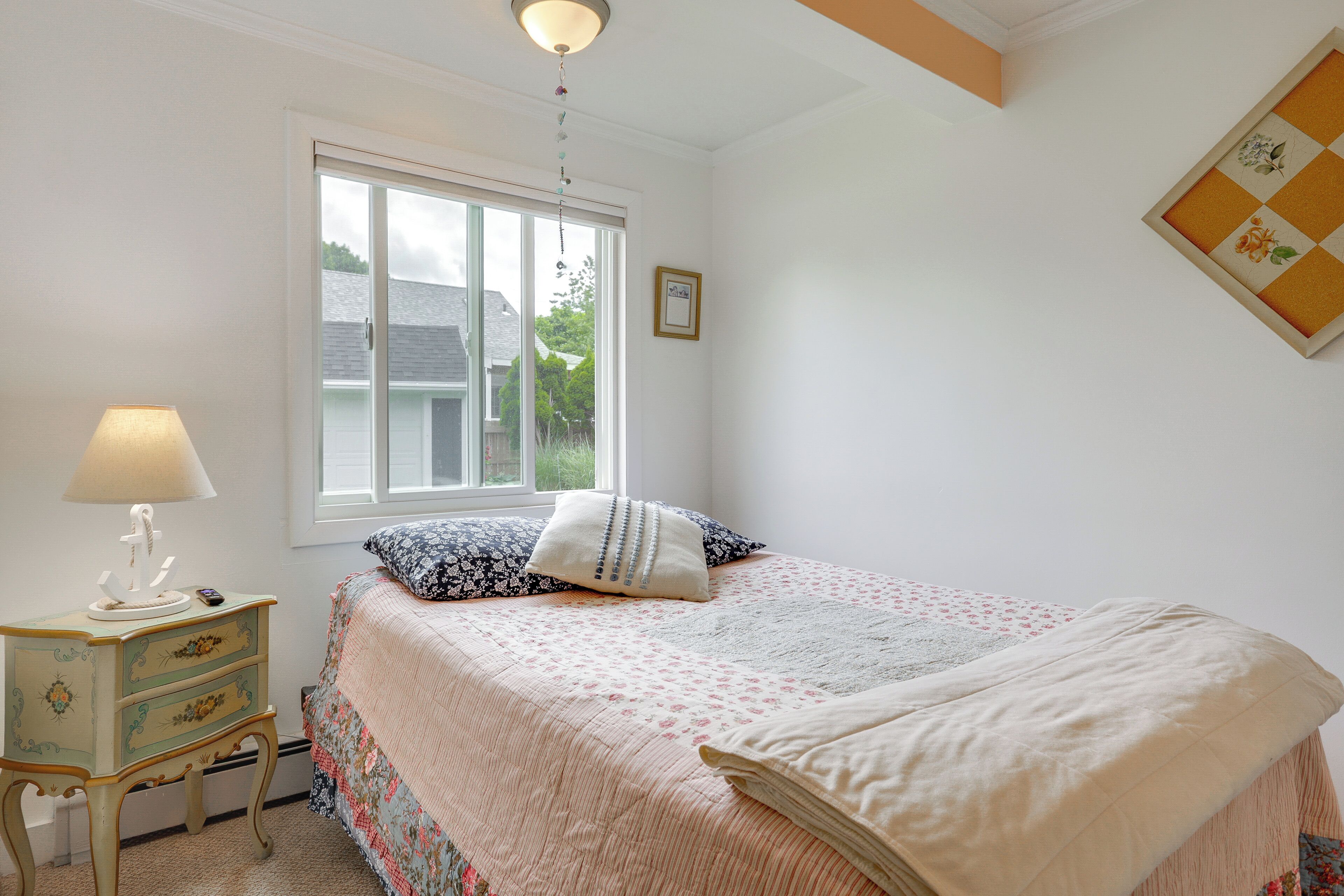 A bedroom with a bed, a nightstand, a lamp, a window, and a wall-mounted picture.