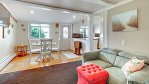 Amplia sala de estar con un sofá verde, un reposapiés rojo y una mesa de comedor con sillas.