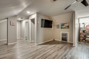 A spacious room with a wooden floor, a flat-screen TV mounted on the wall, and a fireplace.